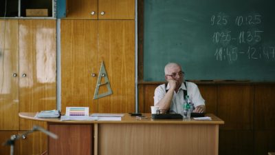 A teacher sits at his desk in a classroom.