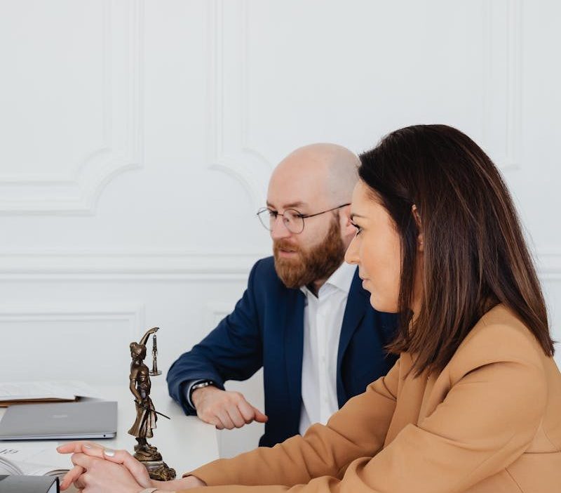 Man and woman discussing legal documents indoors, featuring Lady Justice statue.