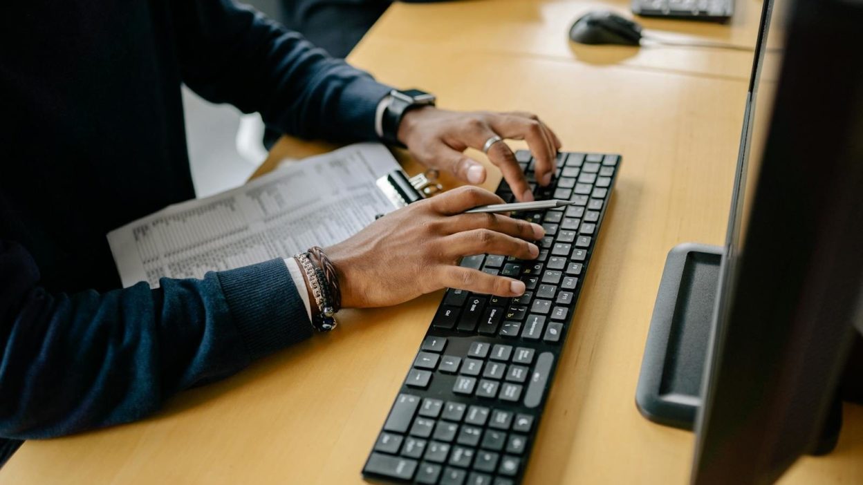 Close-up of hands typing on a keyboard in an office setting with clipboard nearby.