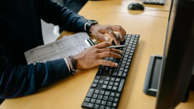 Close-up of hands typing on a keyboard in an office setting with clipboard nearby.